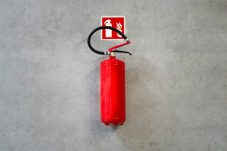 Roter Feuerlöscher mit Notausgangsschild an einer Wand - Handfeuerlöscher.