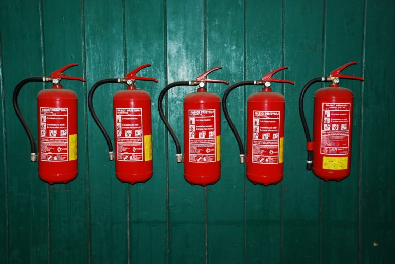 Reihe von Feuerlöschern an grüner Wand montiert.
