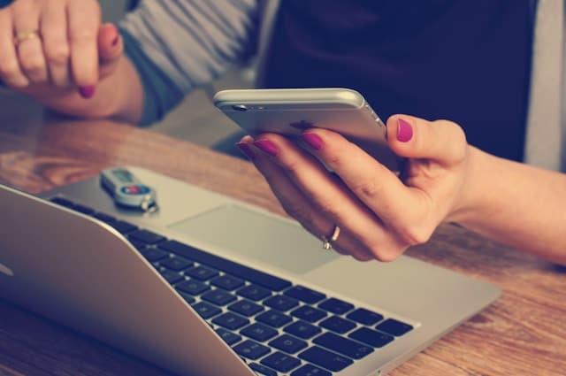 Person nutzt Smartphone neben Laptop.
