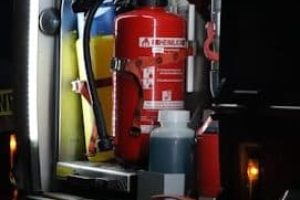 Nahaufnahme eines roten Feuerlöschers vom Typ 'Schlauchlöscher' in einem Einsatzfahrzeug, umgeben von weiteren Ausrüstungsgegenständen wie Schläuchen und Flüssigkeitsbehältern.